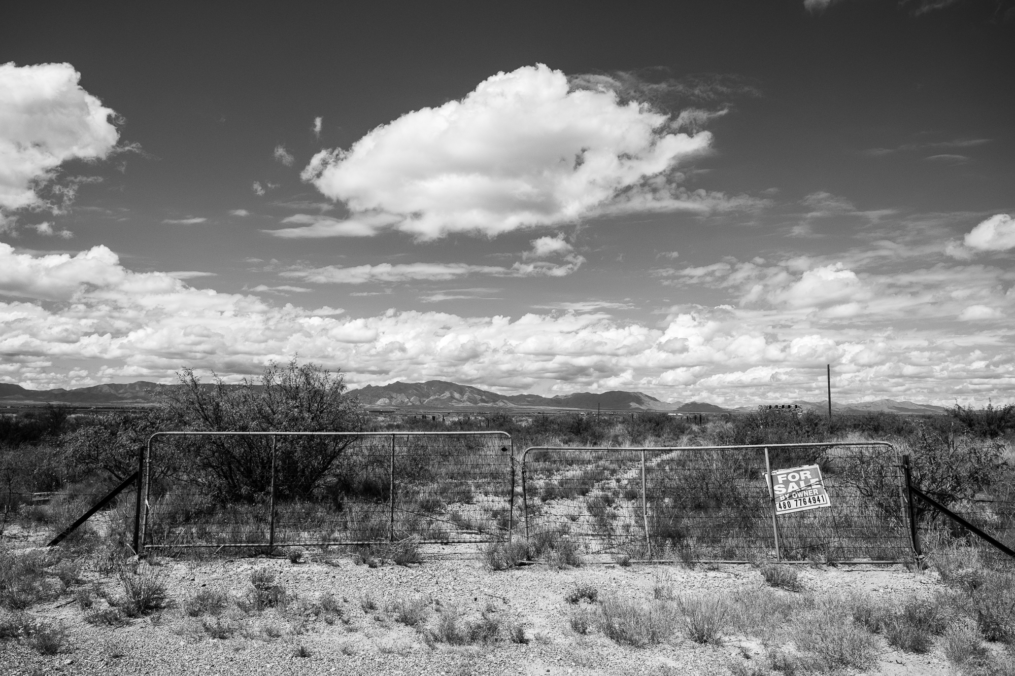 a dry-looking plot of land with a chain link fence and for sale sign