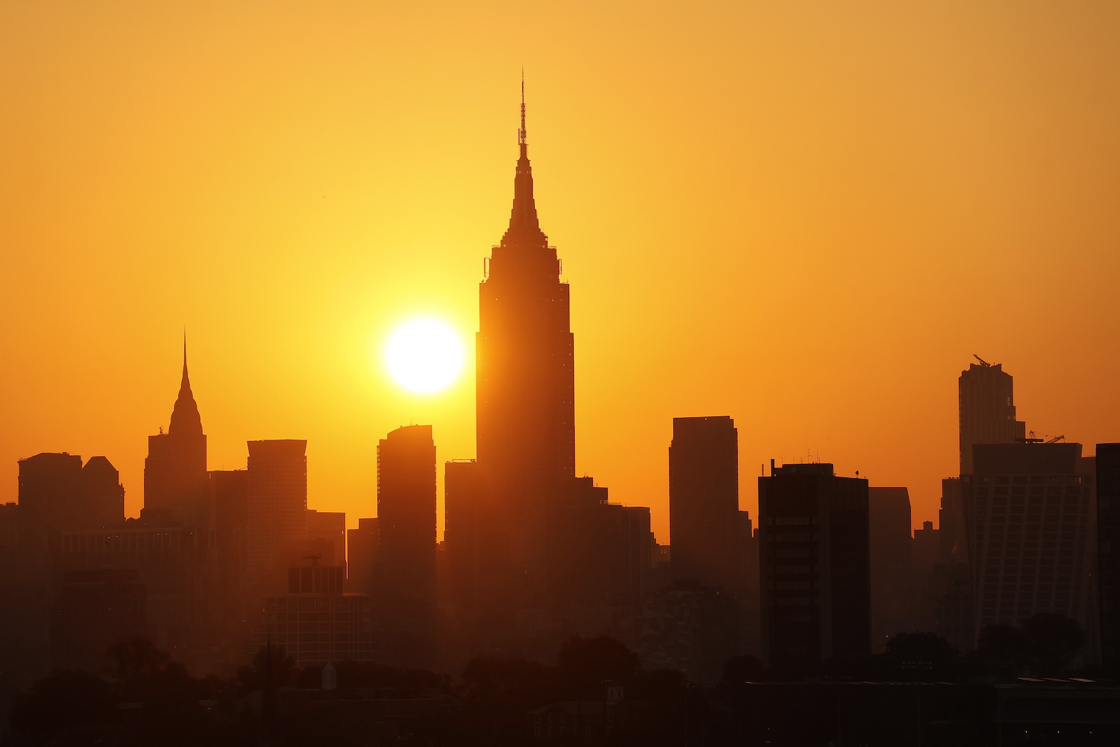 A yellow sun rises against a dark New York City skyline, with the Empire State Building in the center