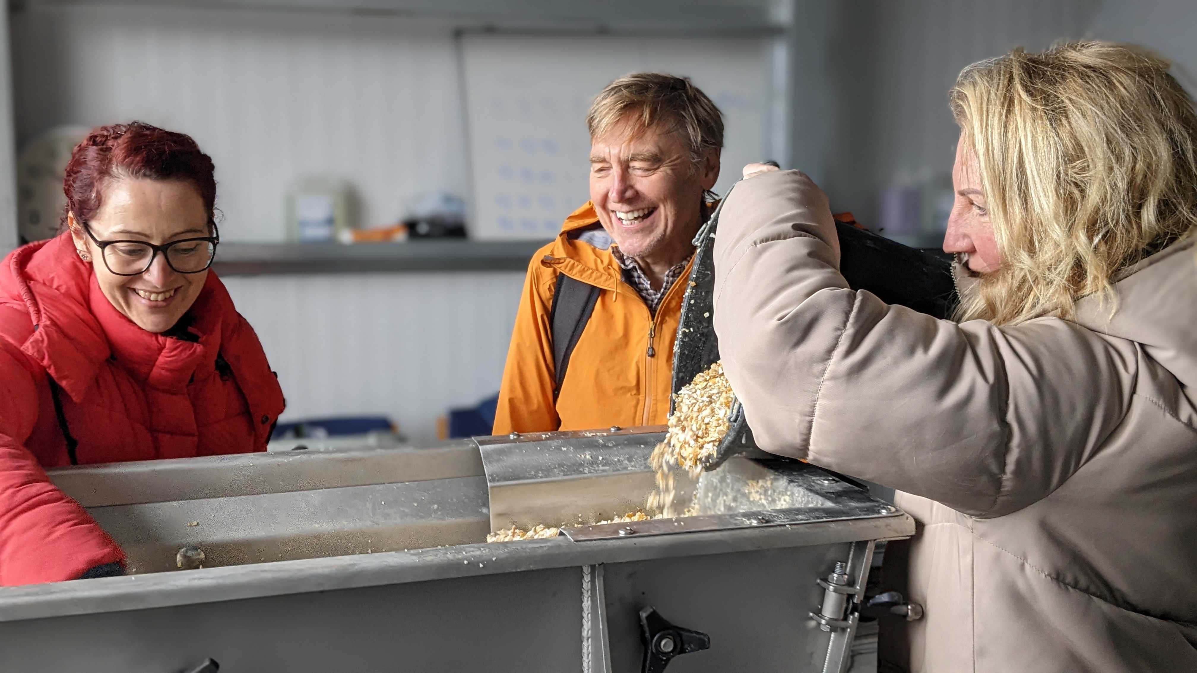 A group of people laughing as they pour shells into a container.